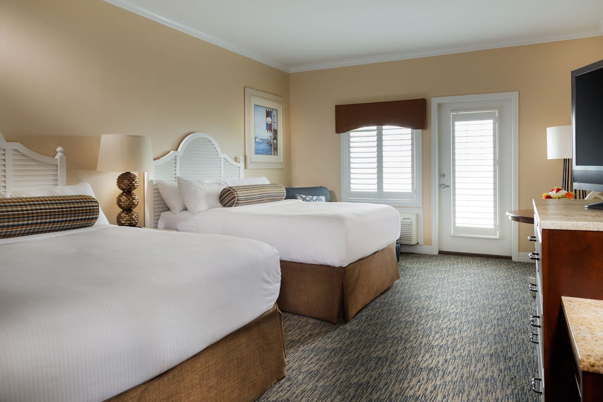 A hotel room with two beds, a desk, a TV, and a window with blinds.