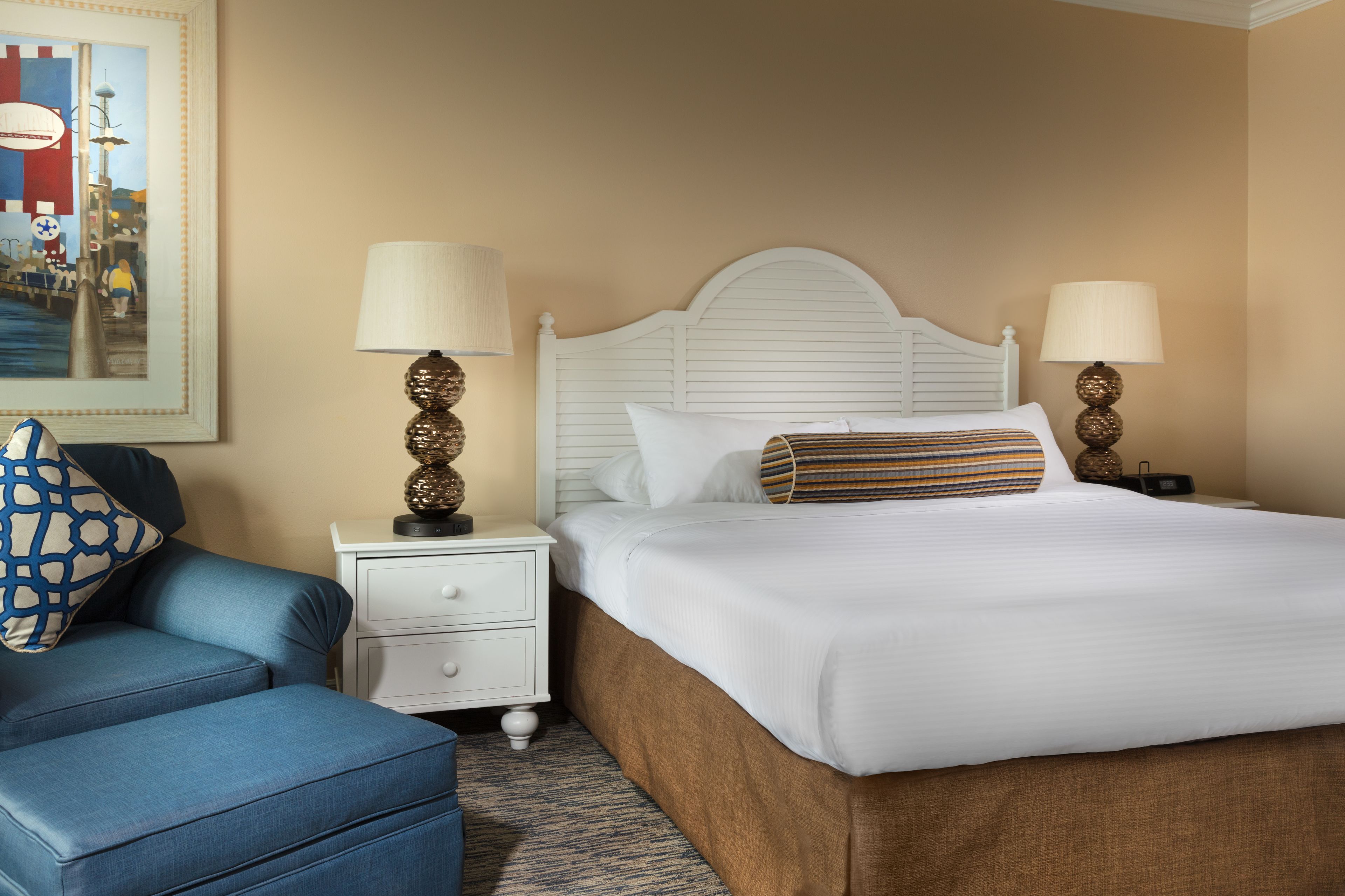 A neatly arranged hotel room with a bed, a blue armchair, a white nightstand, and a lamp.