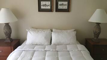 A neatly made bed with white bedding, two framed fish pictures on the wall, and two wooden nightstands with lamps.