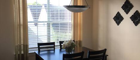 A dining area with a table and chairs, a hanging light fixture, a window with blinds, and decorative wall art.
