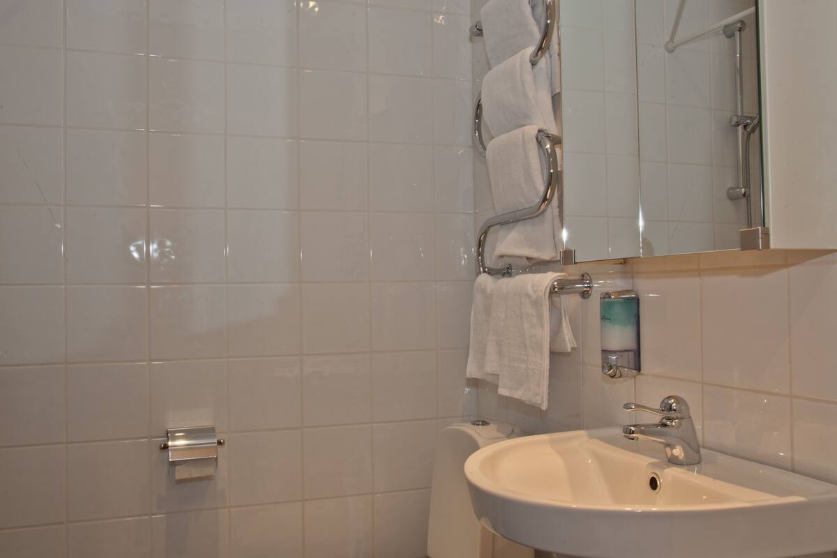 A bathroom with white tiles, a sink, a mirror, and a towel rack.