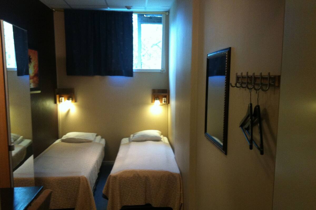 A room with two single beds, a window with curtains, a wall-mounted mirror, and a coat rack with keys.