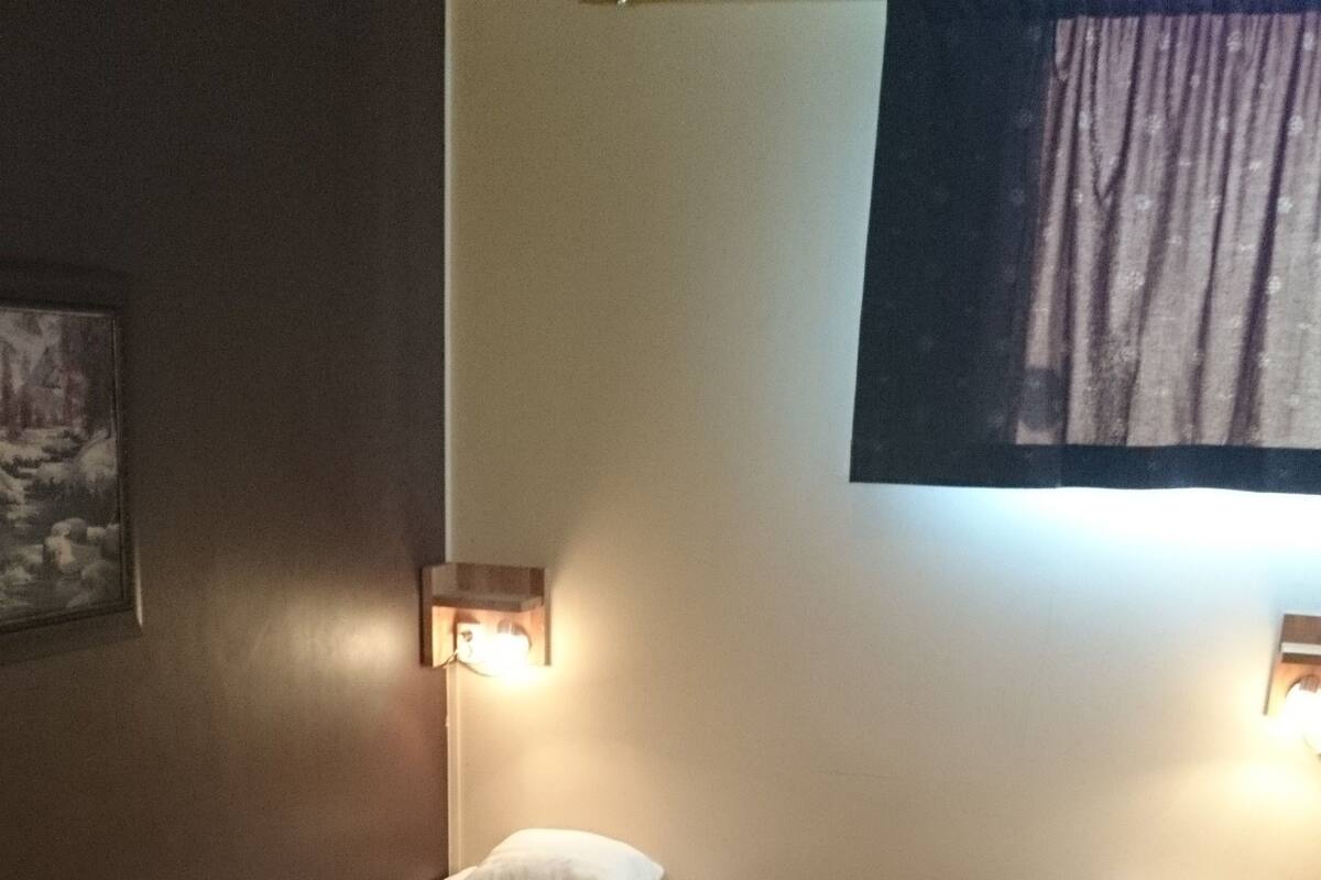 A hotel room with two single beds, a green armchair, a small table, and a wall-mounted TV.