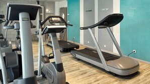 Un gimnasio con cintas de correr y elípticas, suelo de madera y paredes color turquesa.