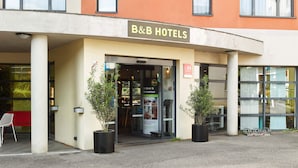 Entrada de un hotel B&B con un letrero, plantas en macetas y un banco rojo en el exterior.