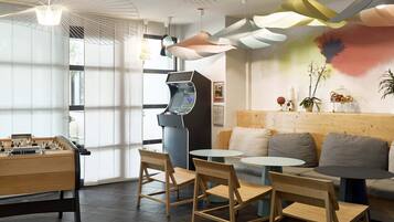Un espace de détente moderne comprenant une table de baby-foot, des chaises en bois, un canapé et une petite table basse.