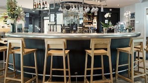 Una zona de bar con un mostrador curvo, taburetes de madera, copas de vino colgantes y una variedad de botellas y adornos.