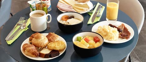 Mesa posta com itens de café da manhã, incluindo croissants, waffles, frutas e uma xícara de café.