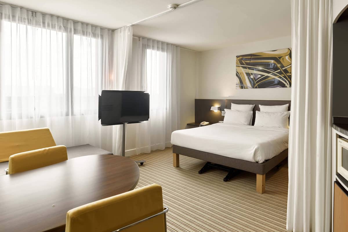 A hotel room with a bed, a desk, a chair, a TV, and a painting on the wall.