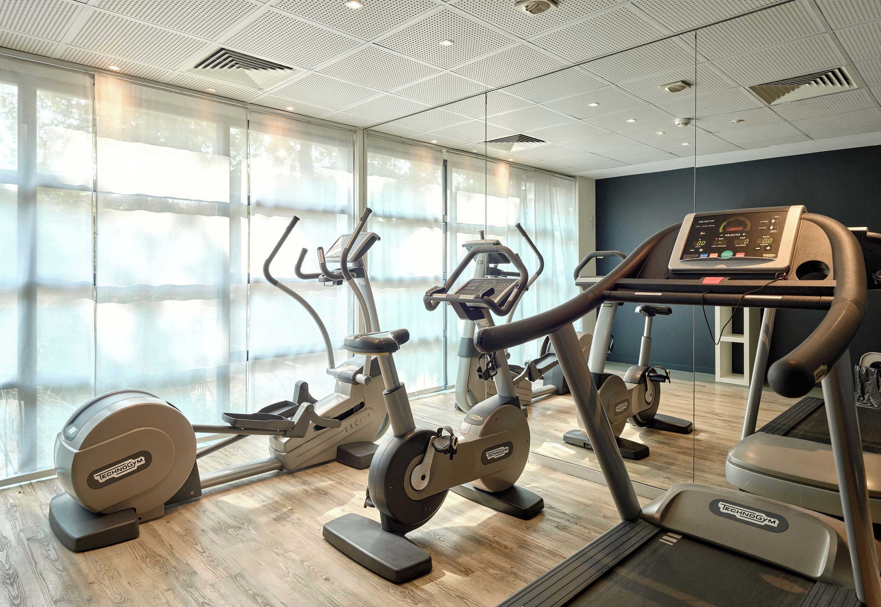 Une salle de sport équipée de divers appareils de cardio, dotée de grandes fenêtres et d’un design moderne au niveau du plafond.