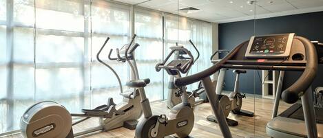 Un gimnasio con diversas máquinas de cardio, amplios ventanales y un diseño moderno en el techo.