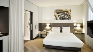Una habitación de hotel moderna con una cama grande, televisor, escritorio con lámpara y un cuadro en la pared.