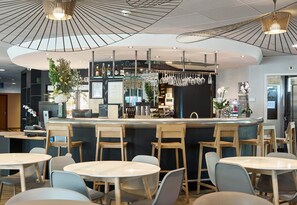 Un espace bar moderne avec un comptoir incurvé, des chaises et des tables en bois. On y trouve des verres suspendus, ainsi qu’une variété de bouteilles et de verres disposés sur le comptoir.