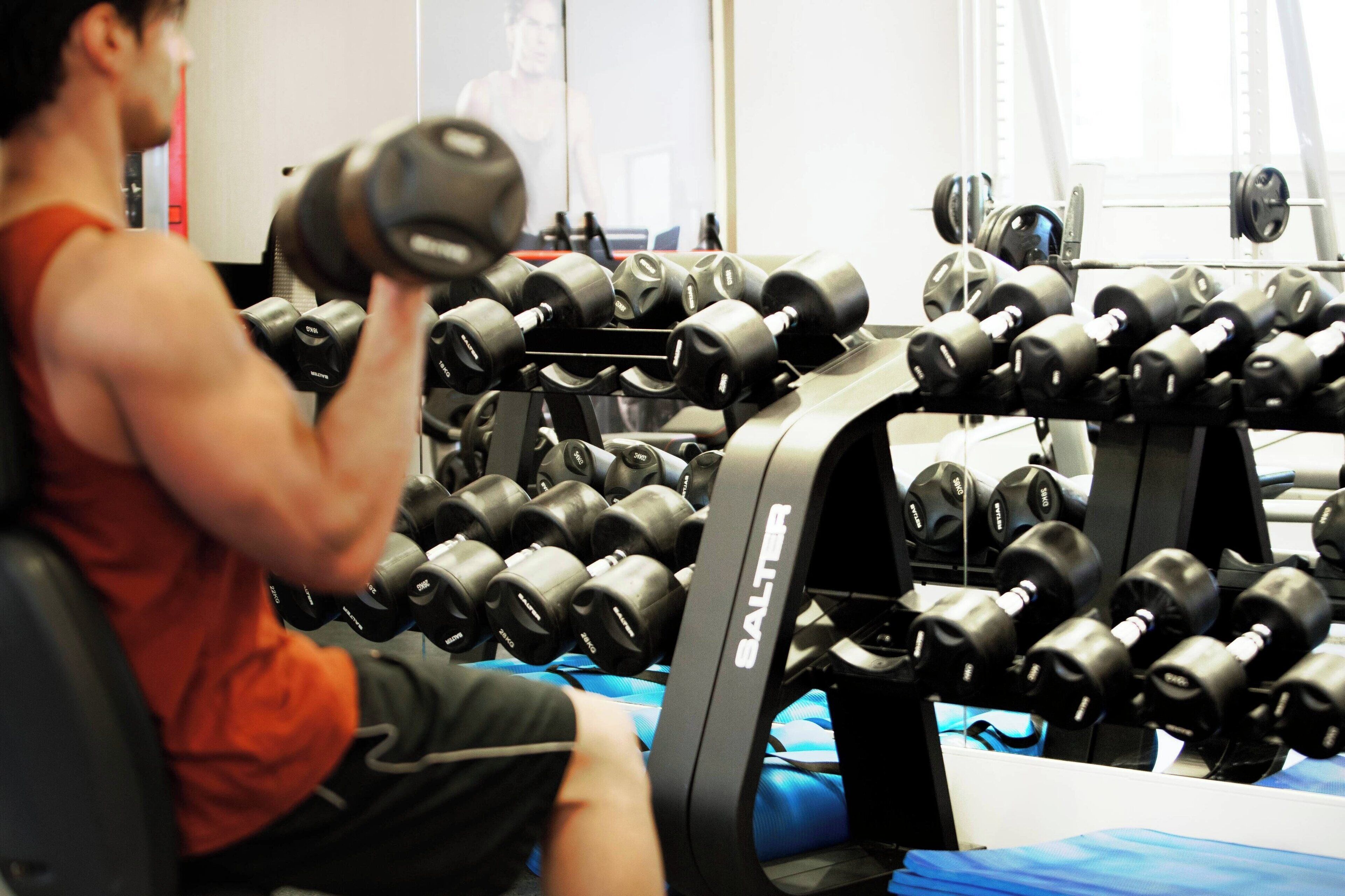 Een sportschool met een man die gewichten heft, een dumbbellrek en trainingsapparatuur.