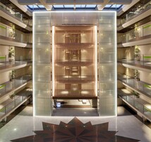 Ein mehrgeschossiges Atrium mit Glasgeländern, einer zentralen Holzkonstruktion und einem geometrischen Bodenmuster.