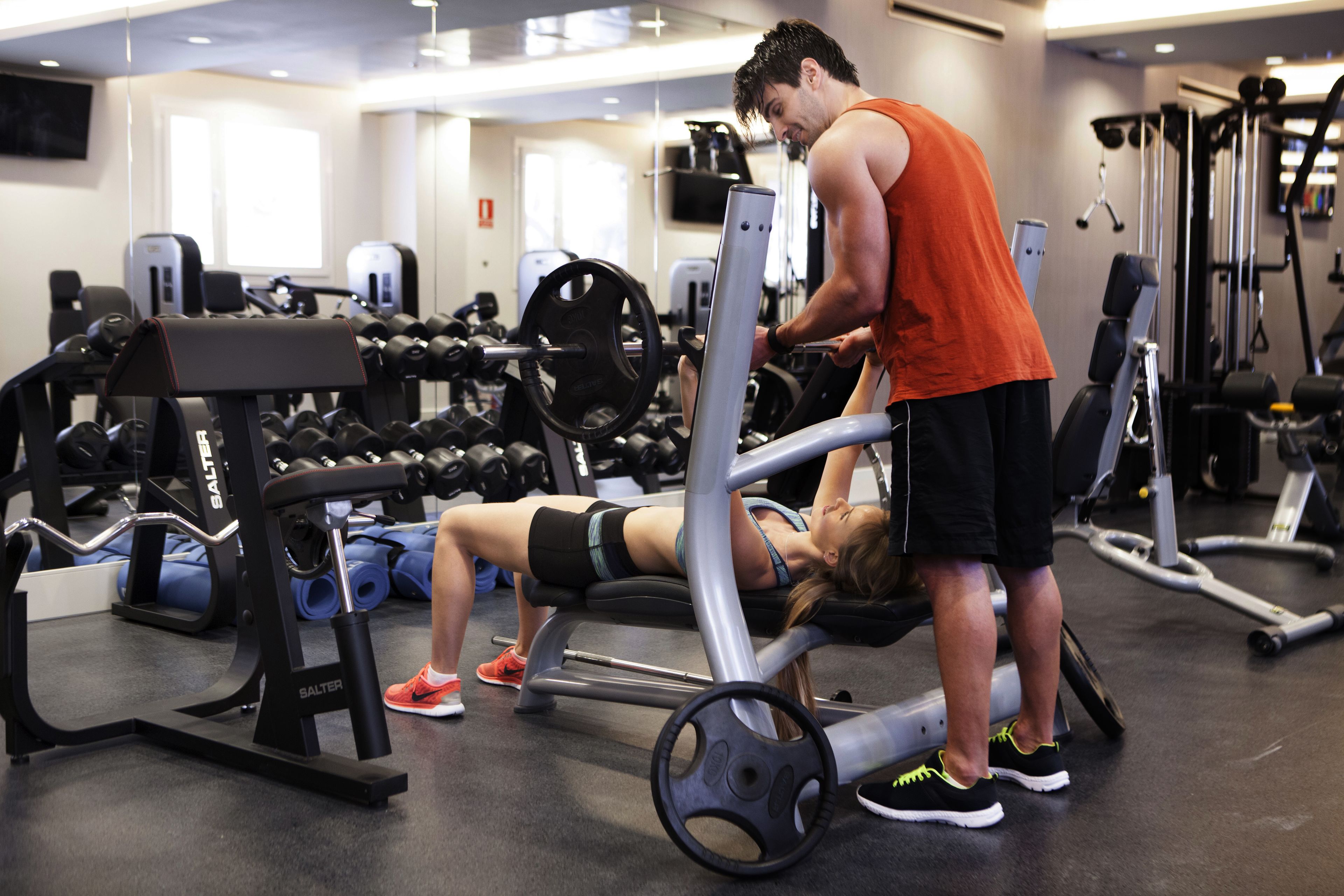 Un gimnasio con diferentes equipos de ejercicio, incluyendo mancuernas, una prensa de banca y una máquina de pesas.