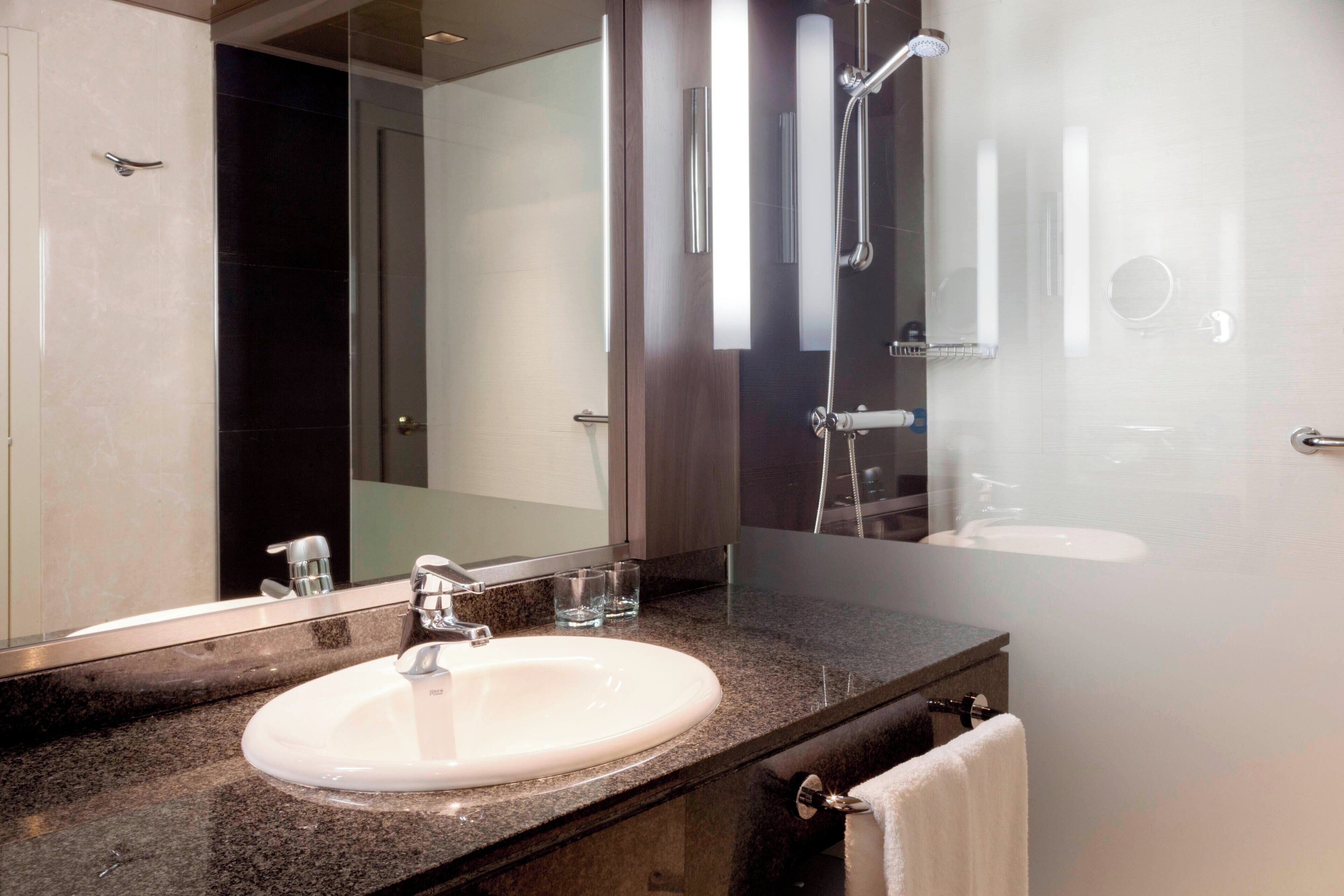 Un baño moderno con un lavabo blanco, un espejo grande y una cabina de ducha de vidrio.