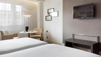 Habitació d'hotel amb dos llits, una televisió penjada a la paret, una taula petita amb una làmpada i una cadira.