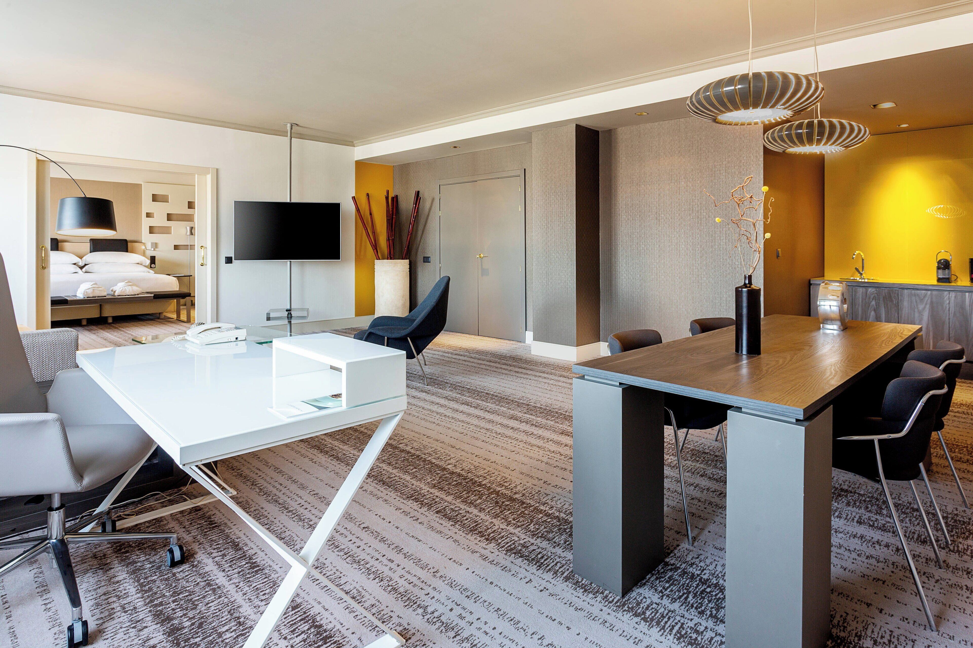A modern hotel room with a large bed, a desk, and a dining area.