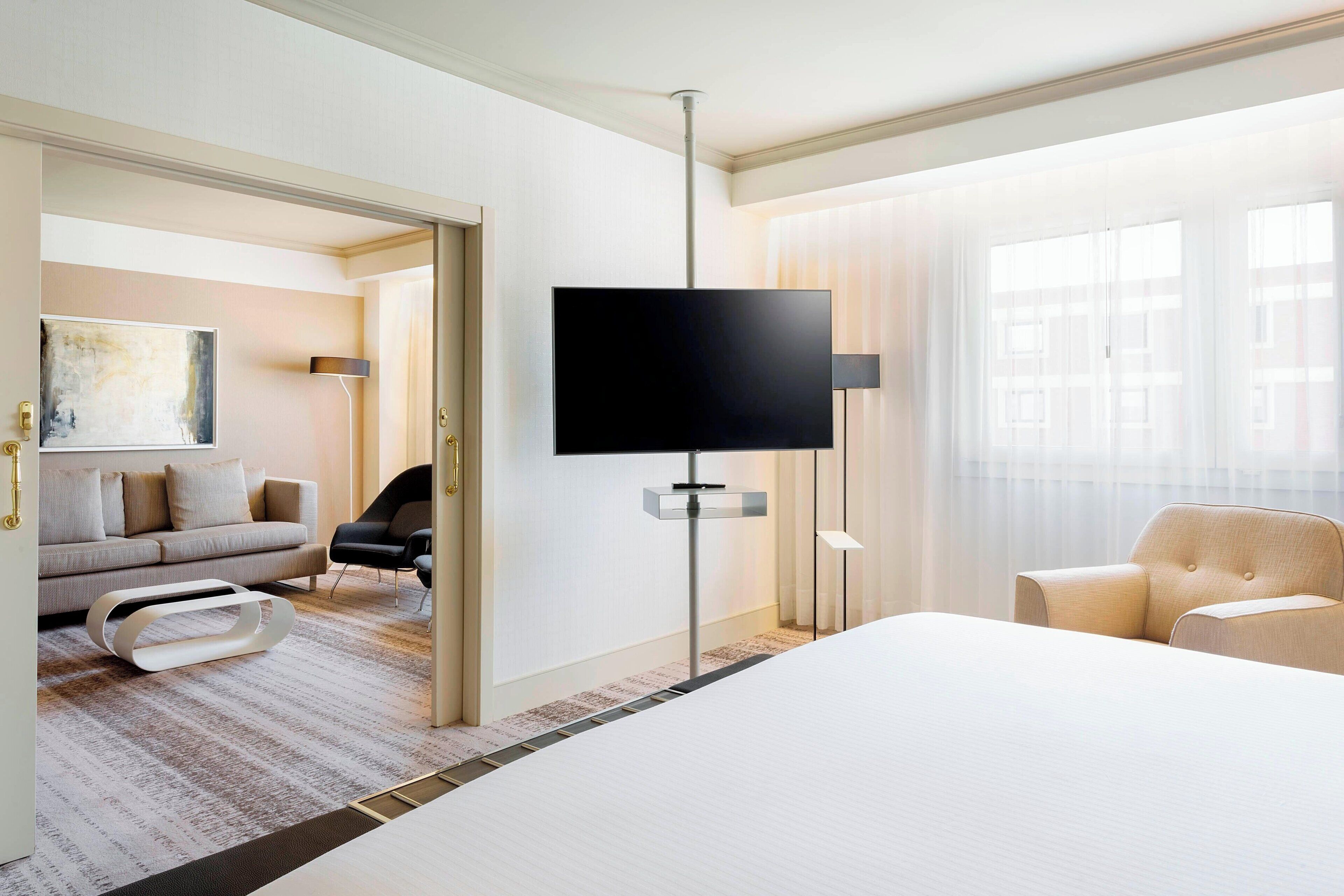 A modern hotel room with a large bed, a flat-screen TV mounted on the wall, a sofa, and a chair.