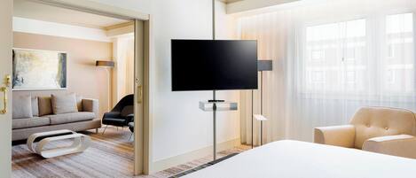 A modern hotel room with a large bed, a flat-screen TV mounted on the wall, a sofa, and a chair.