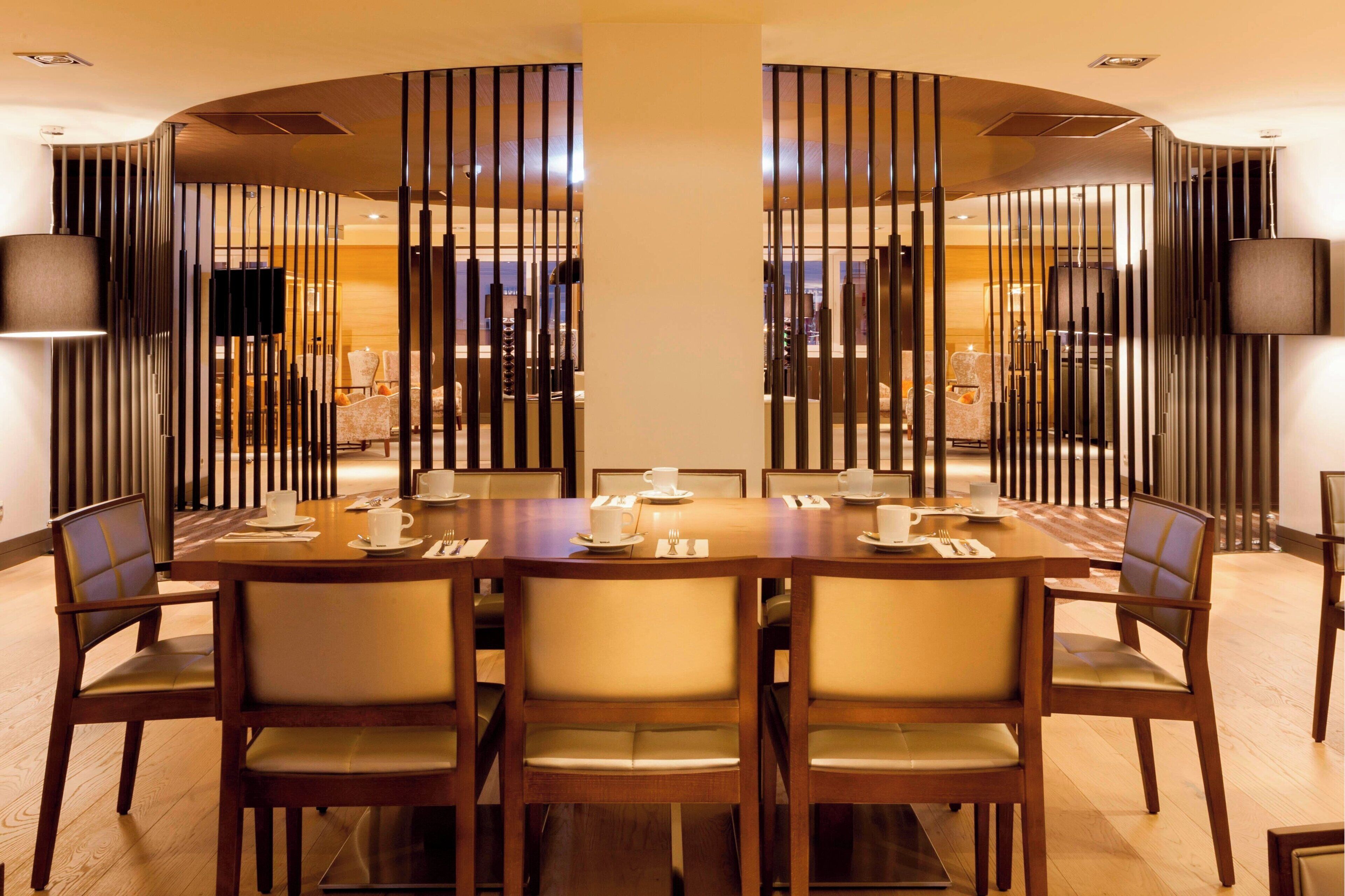 A dining area with a large wooden table set for six, surrounded by chairs with cushioned seats.