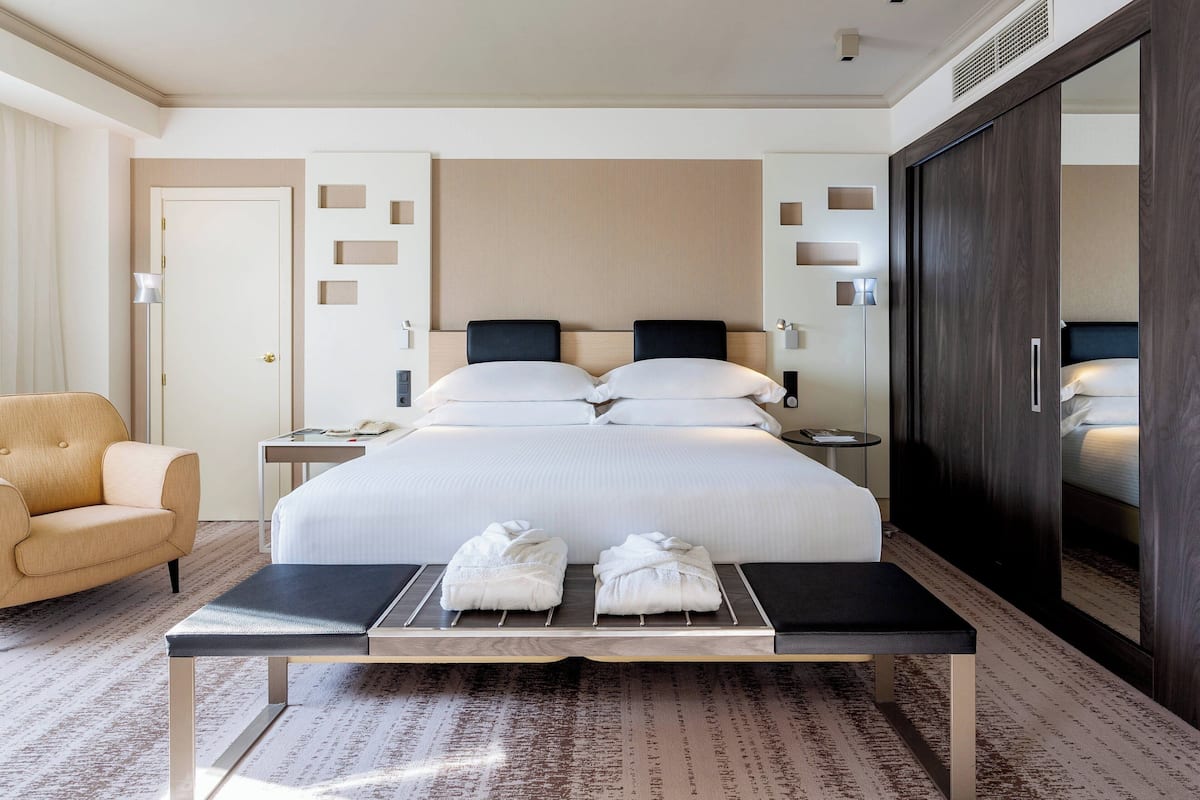 Ein Hotelzimmer mit einem großen Bett, Nachttischen, einer Bank mit Handtüchern, einem Sessel und einem Kleiderschrank.