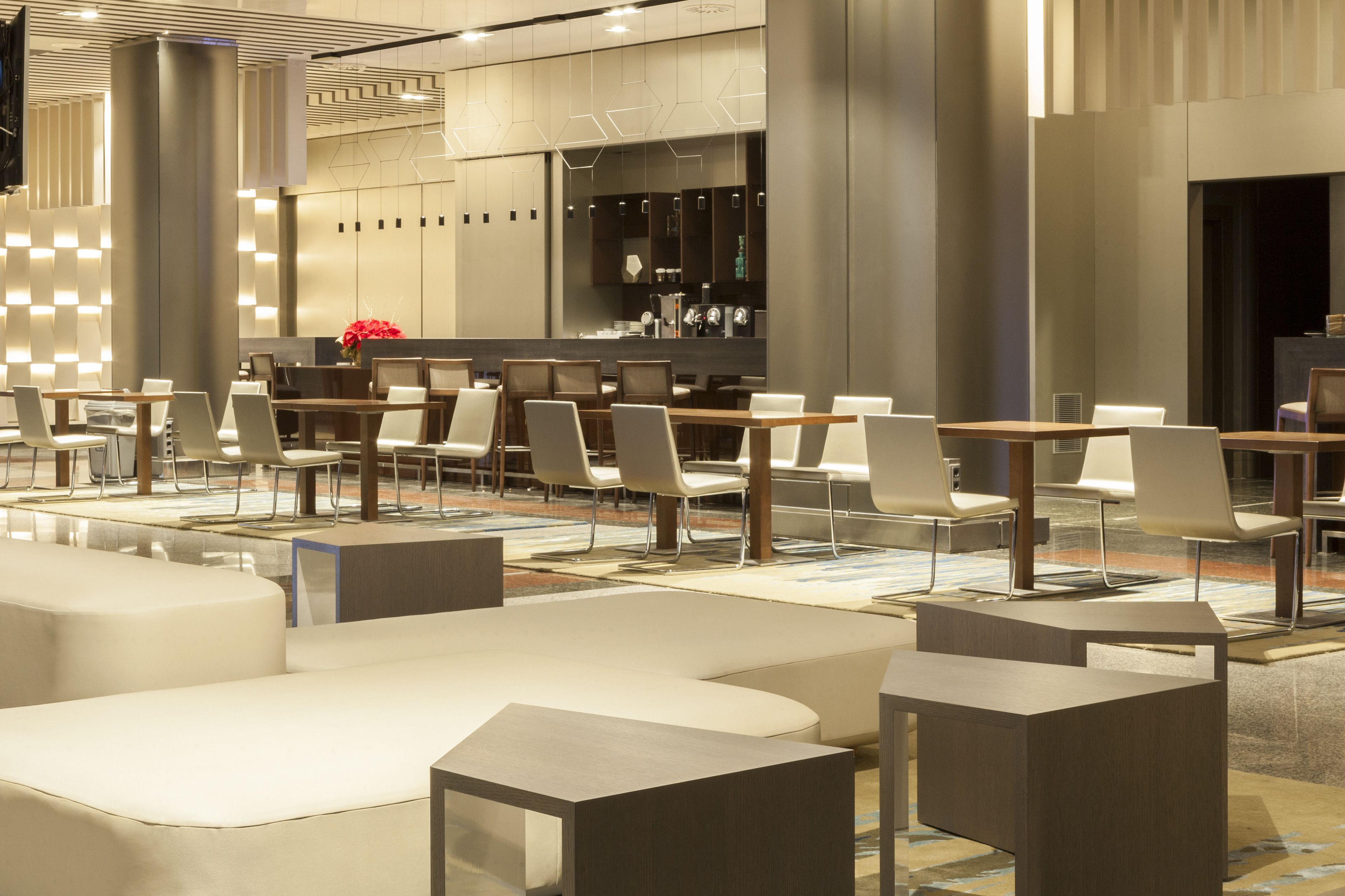 A modern hotel lobby with a mix of seating areas, including sofas and tables, and a bar area with a counter and bar stools.