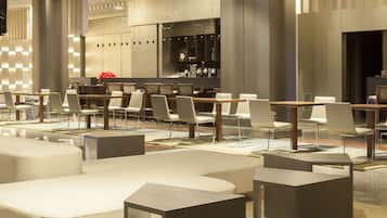 A modern hotel lobby with a mix of seating areas, including sofas and tables, and a bar area with a counter and bar stools.