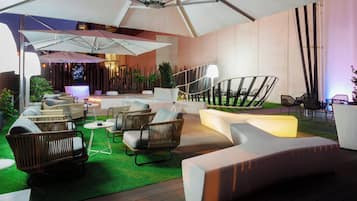 Un espace extérieur aménagé avec des chaises en osier et un canapé blanc, protégé par un grand parasol.