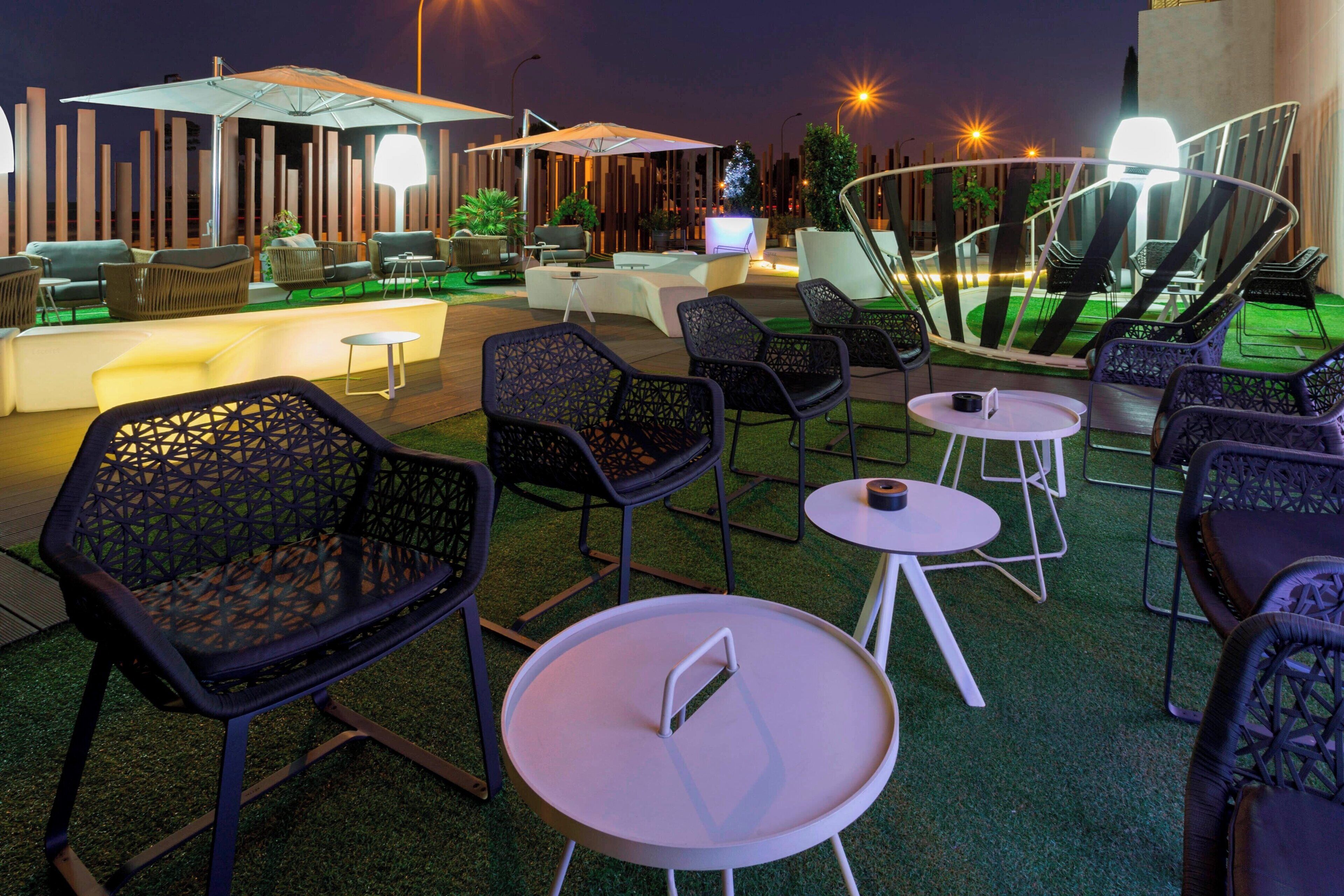 Un espacio al aire libre con mobiliario moderno, que incluye sillas y mesas, y una zona de bar con televisor de pantalla plana.