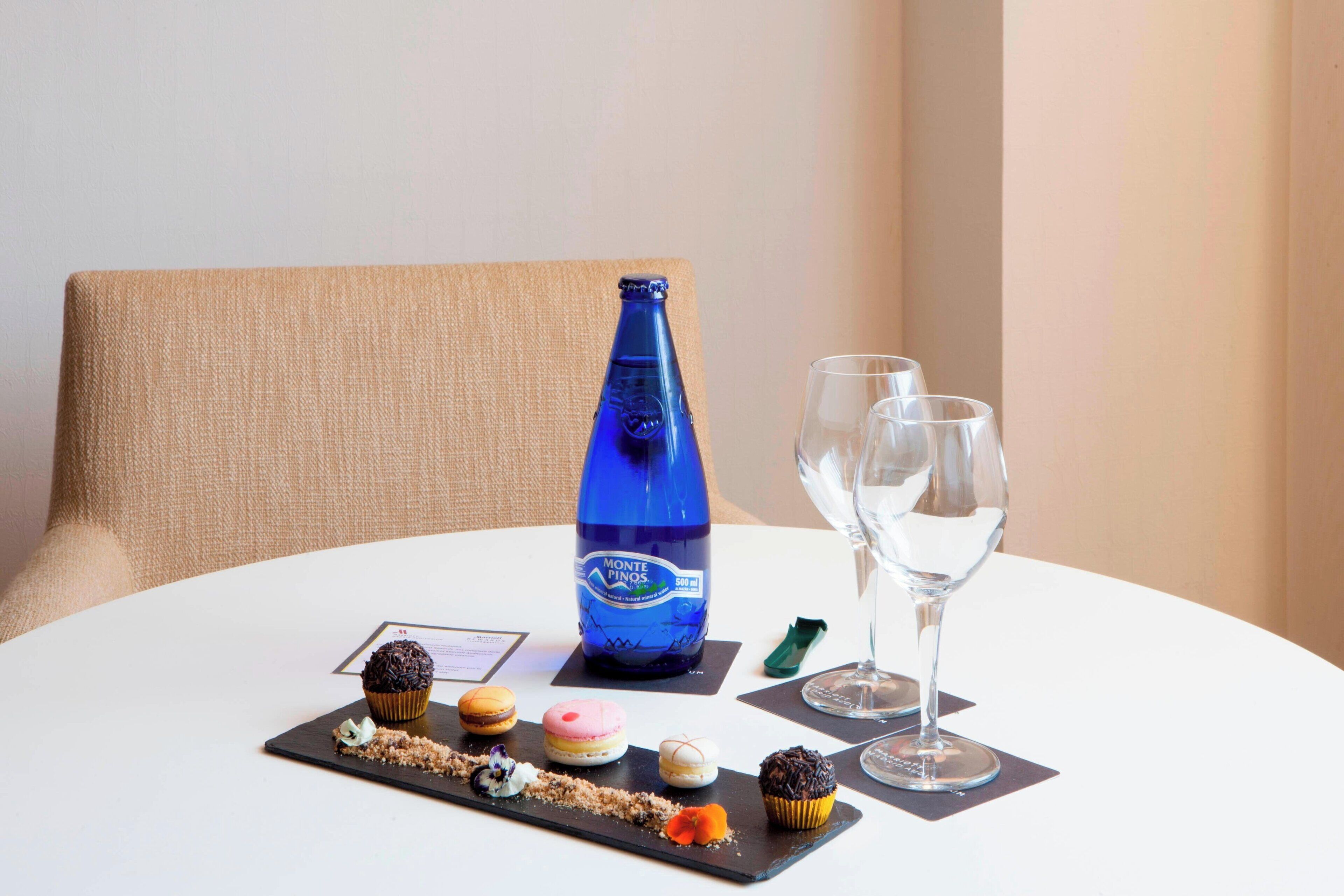 Una mesa con una botella de Monte Finos, dos copas y una bandeja de postres.