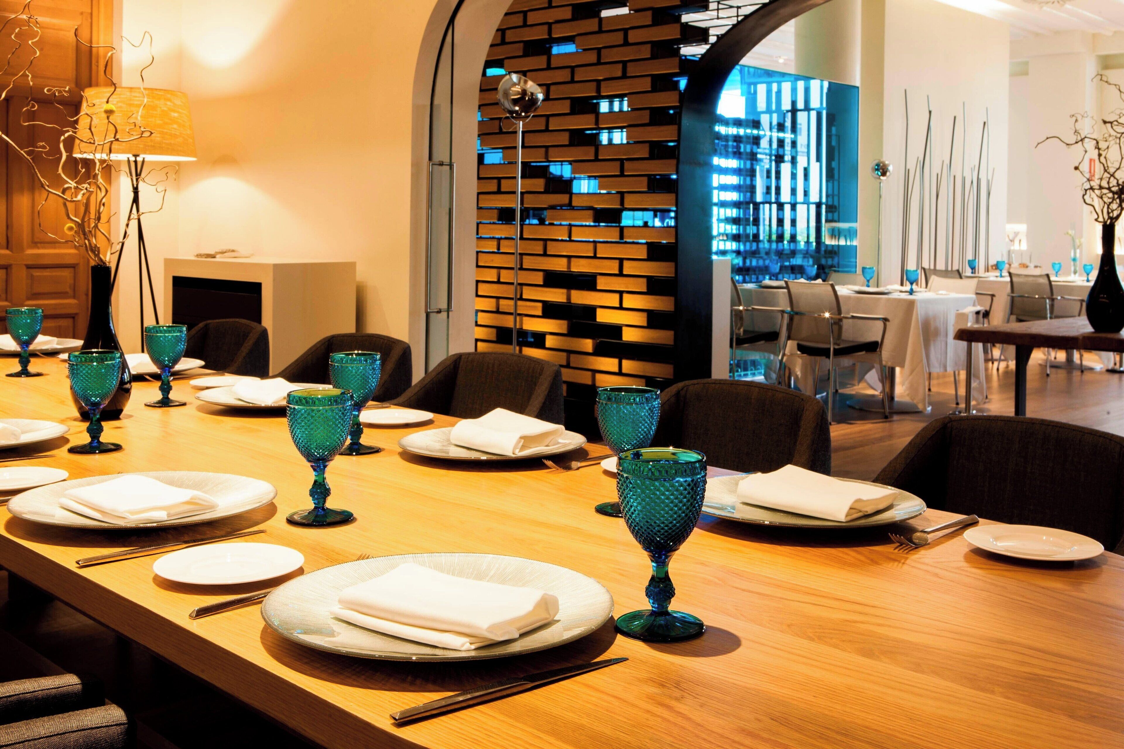 Un comedor con una mesa larga dispuesta para una comida, sillas y una pared de ladrillo moderna al fondo.