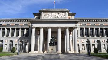 Un gran edificio de arquitectura clásica, con una estatua central, columnas y una bandera.