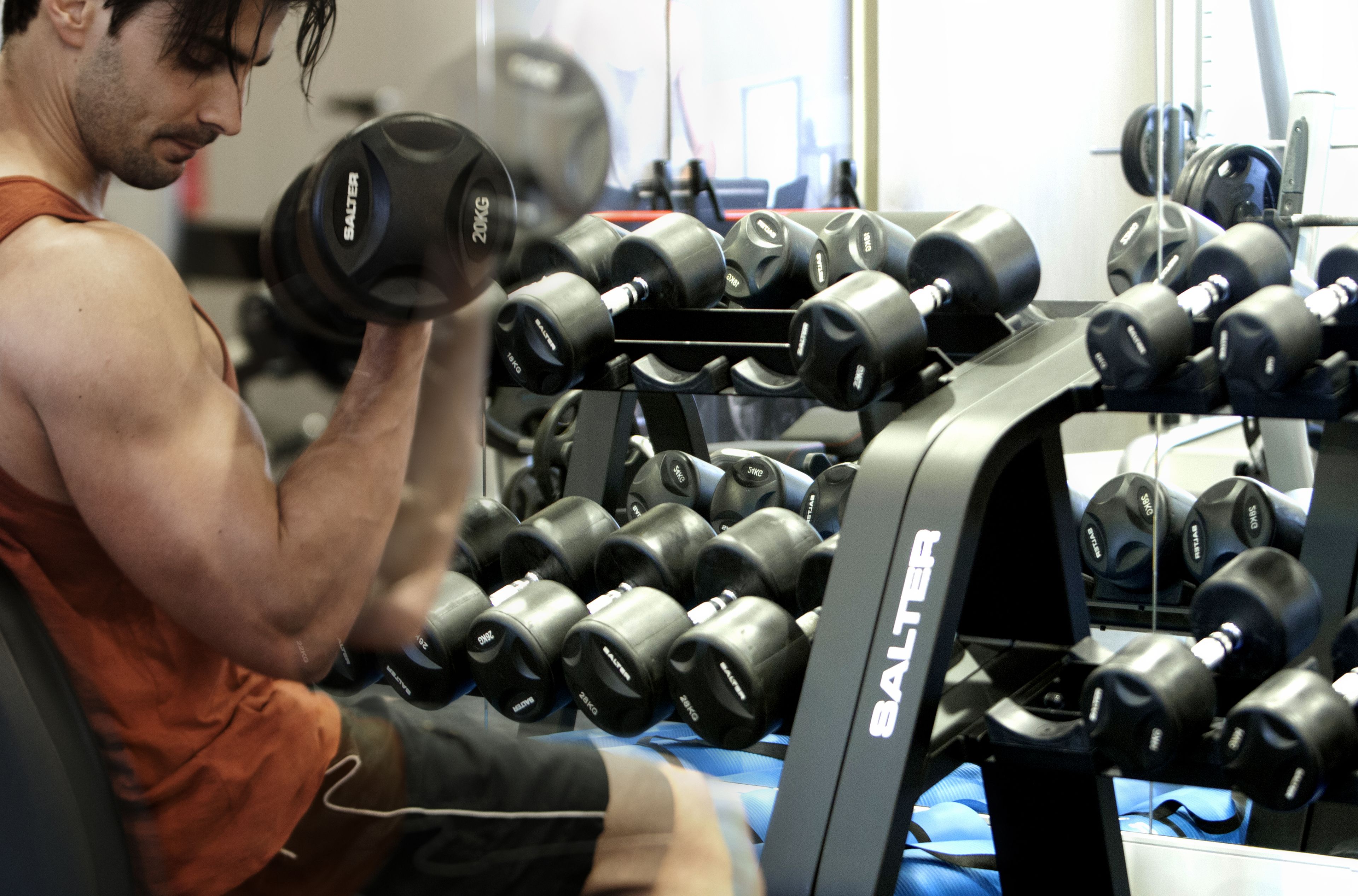 A gym with a man lifting dumbbells, a rack of dumbbells, and weight plates.