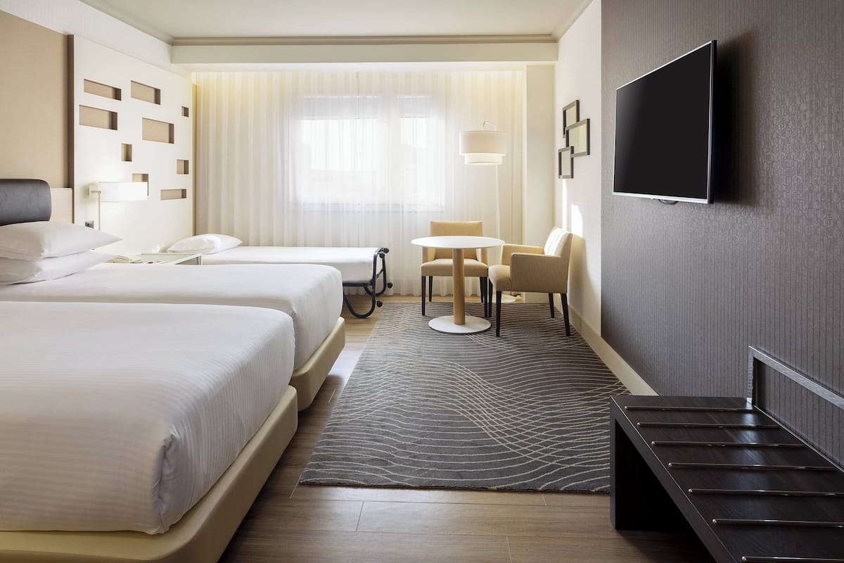 Ein Hotelzimmer mit zwei Betten, einem Fernseher, einem Schreibtisch und einem Sessel.