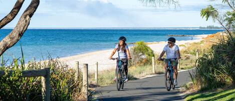 Un sendero pavimentado junto a una playa con dos ciclistas.