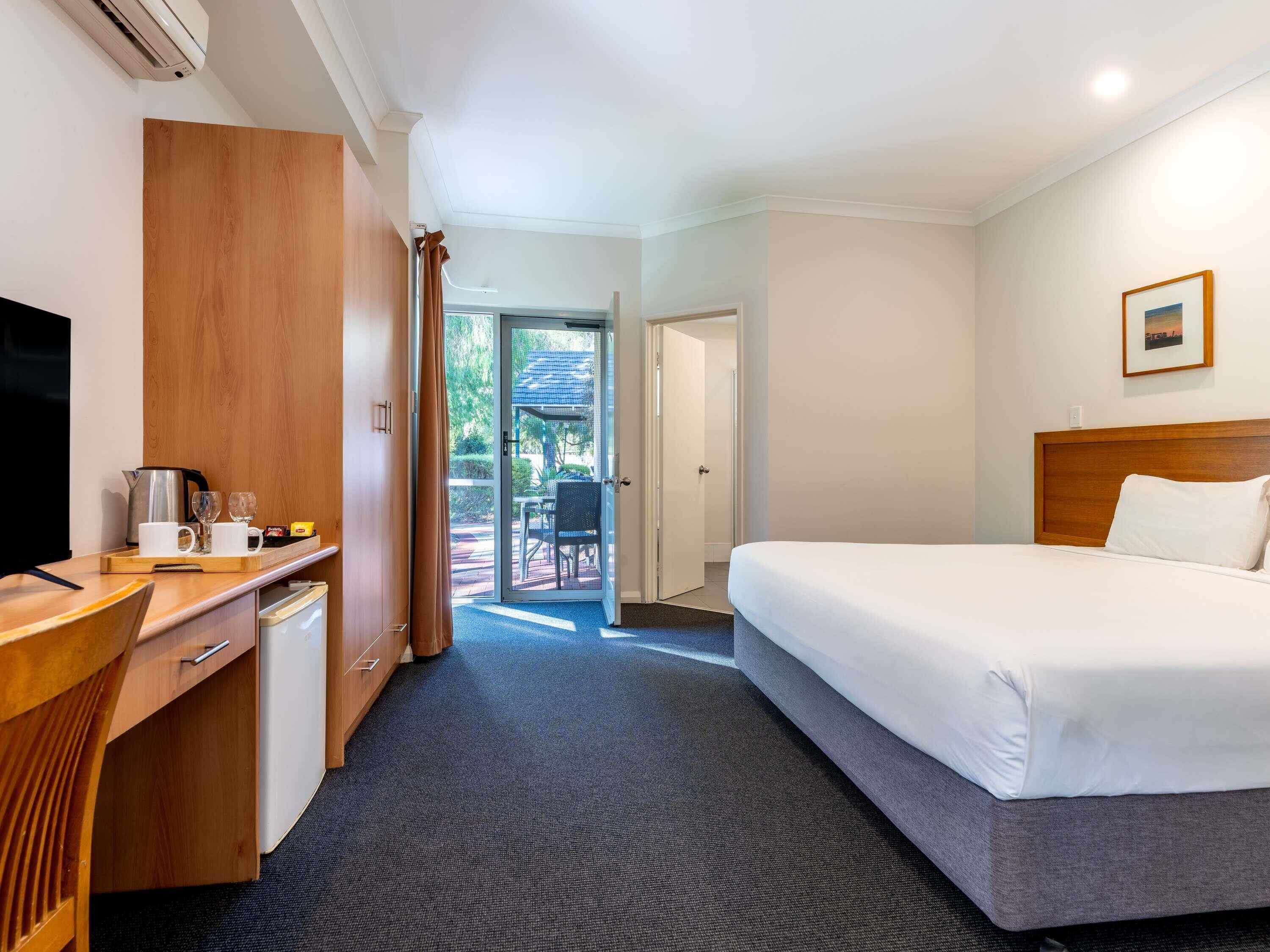 A hotel room with a bed, a desk with a coffee maker, a TV, and a view of the outside.
