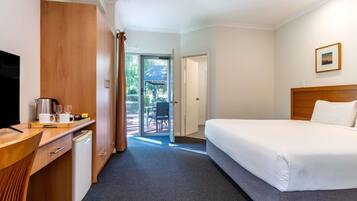 Quarto de hotel com cama, escrivaninha com cafeteira, televisão e vista para o exterior.