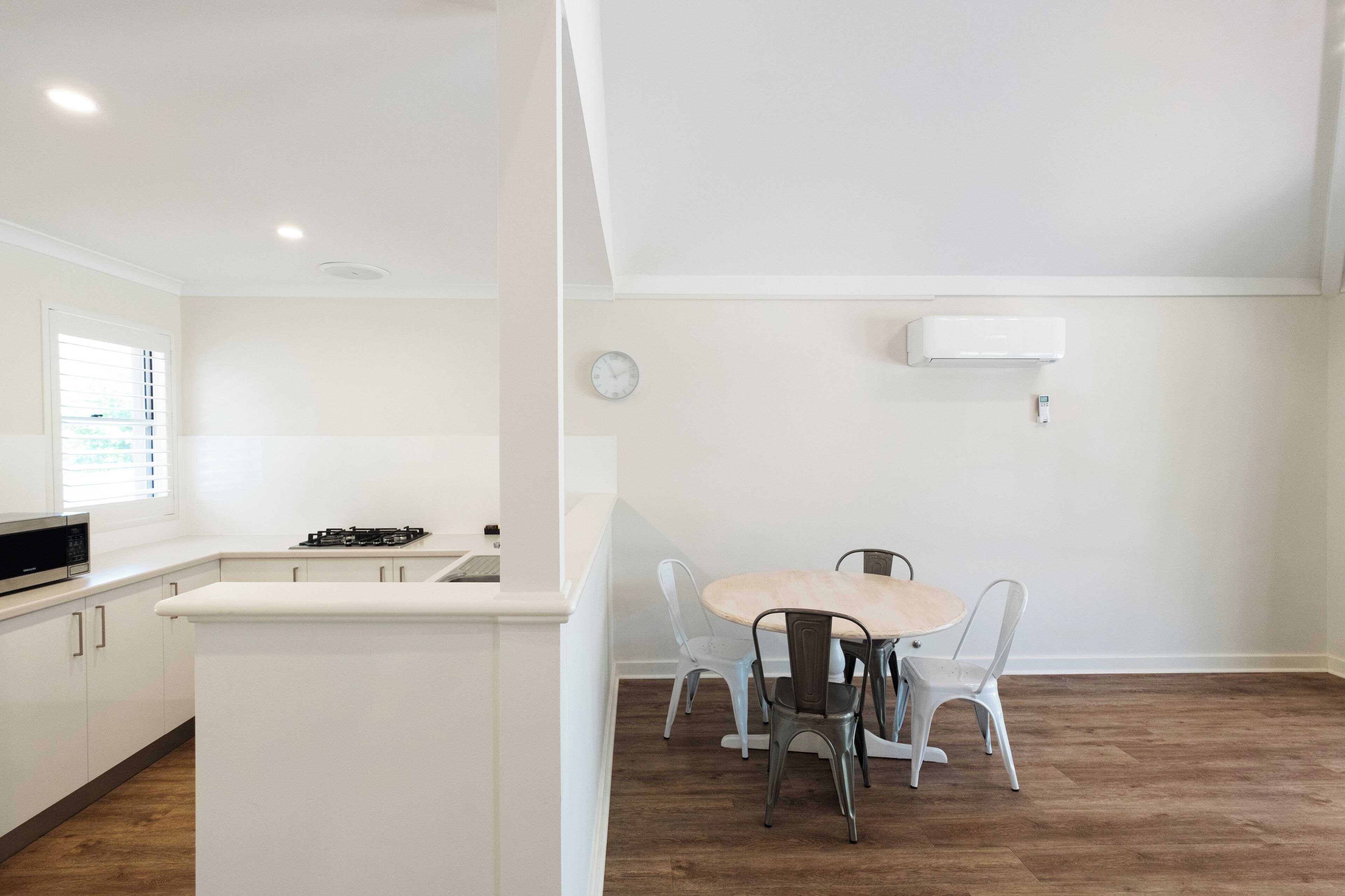Una cocina moderna con armarios blancos, una isla central y un comedor con una mesa redonda y cuatro sillas.