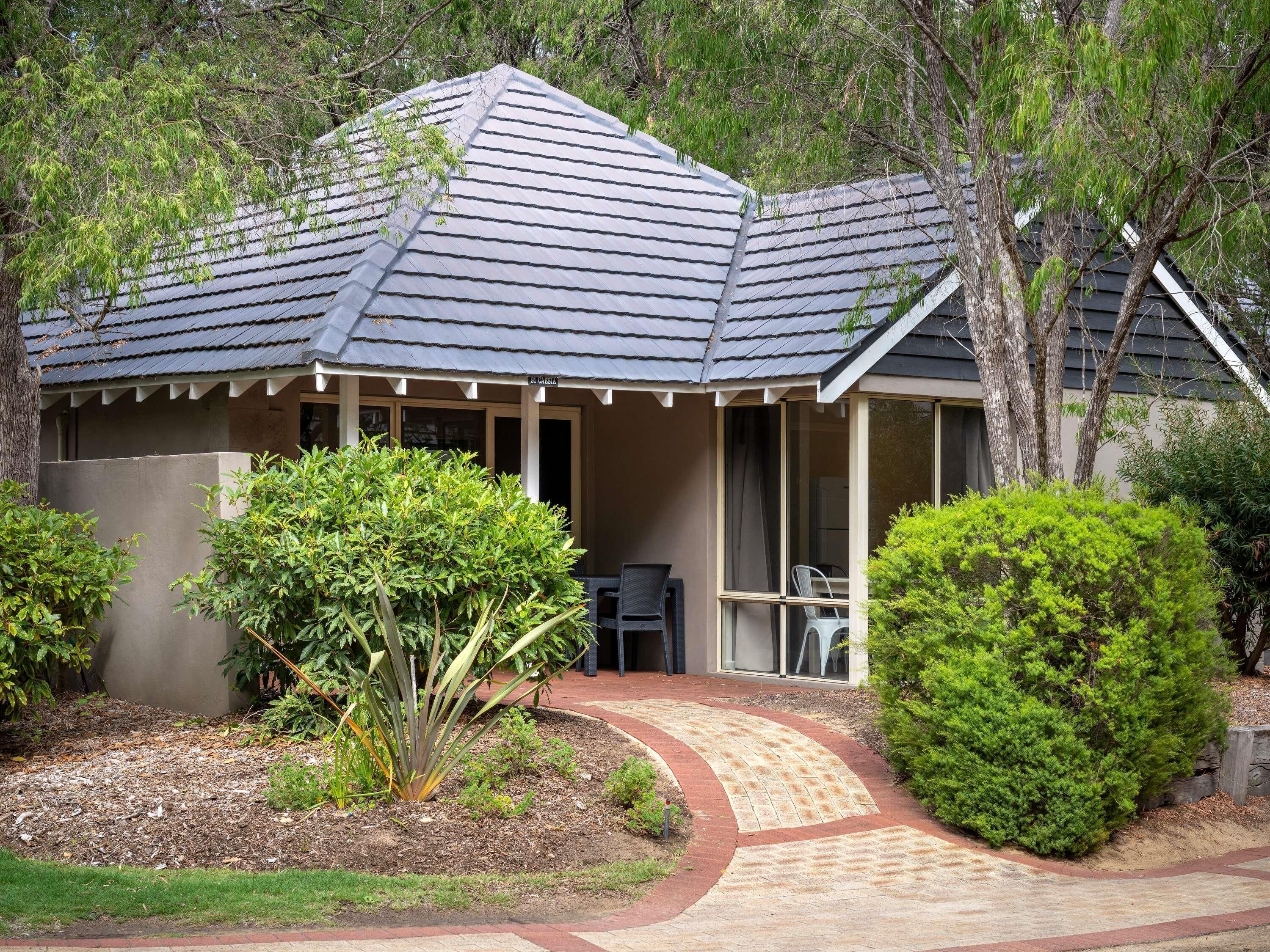 A house with a sloped roof, a covered porch, and a landscaped garden with a pathway leading to the entrance.