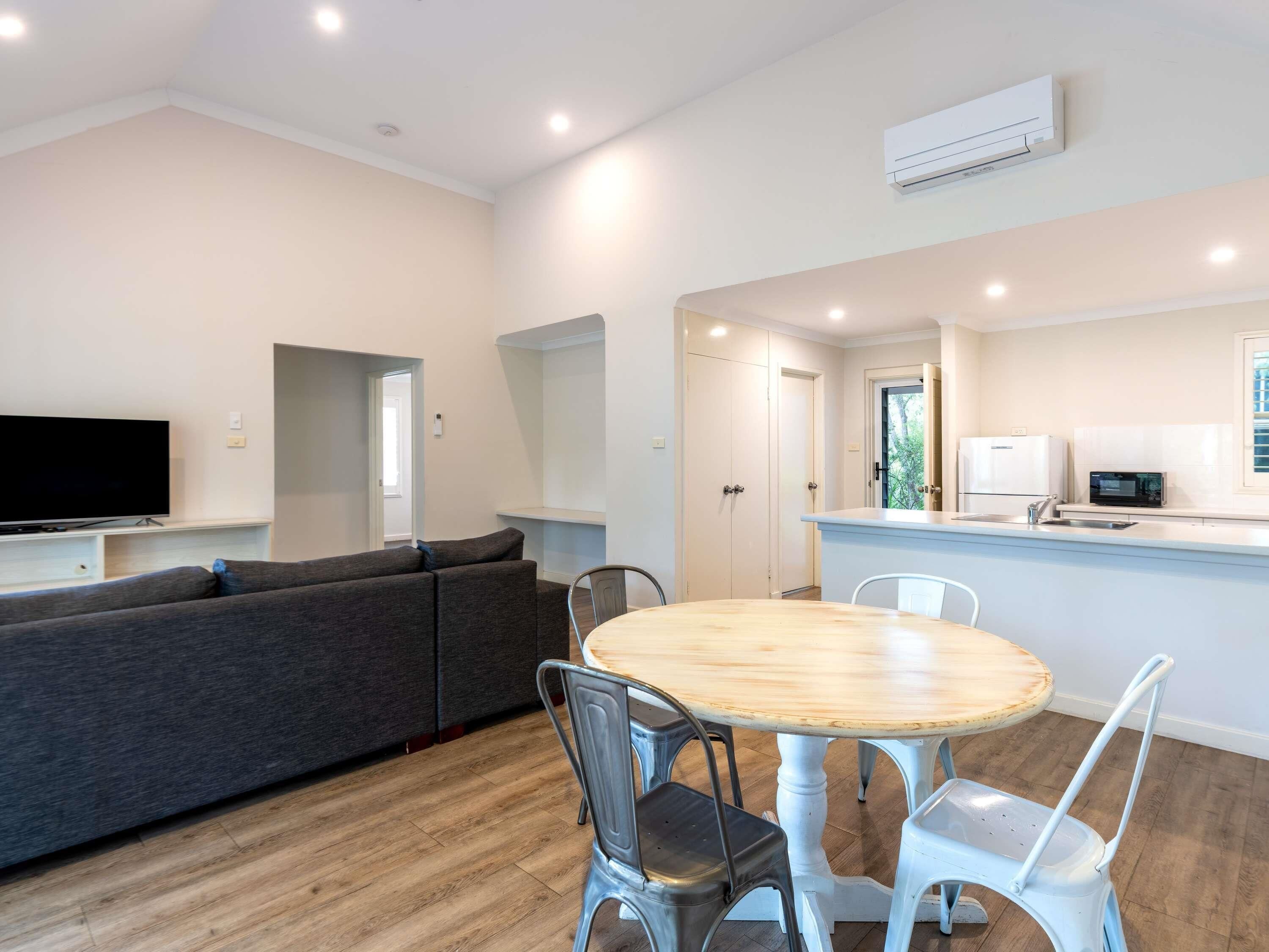 A modern living room with a sofa, a TV, and a dining area with a table and chairs.
