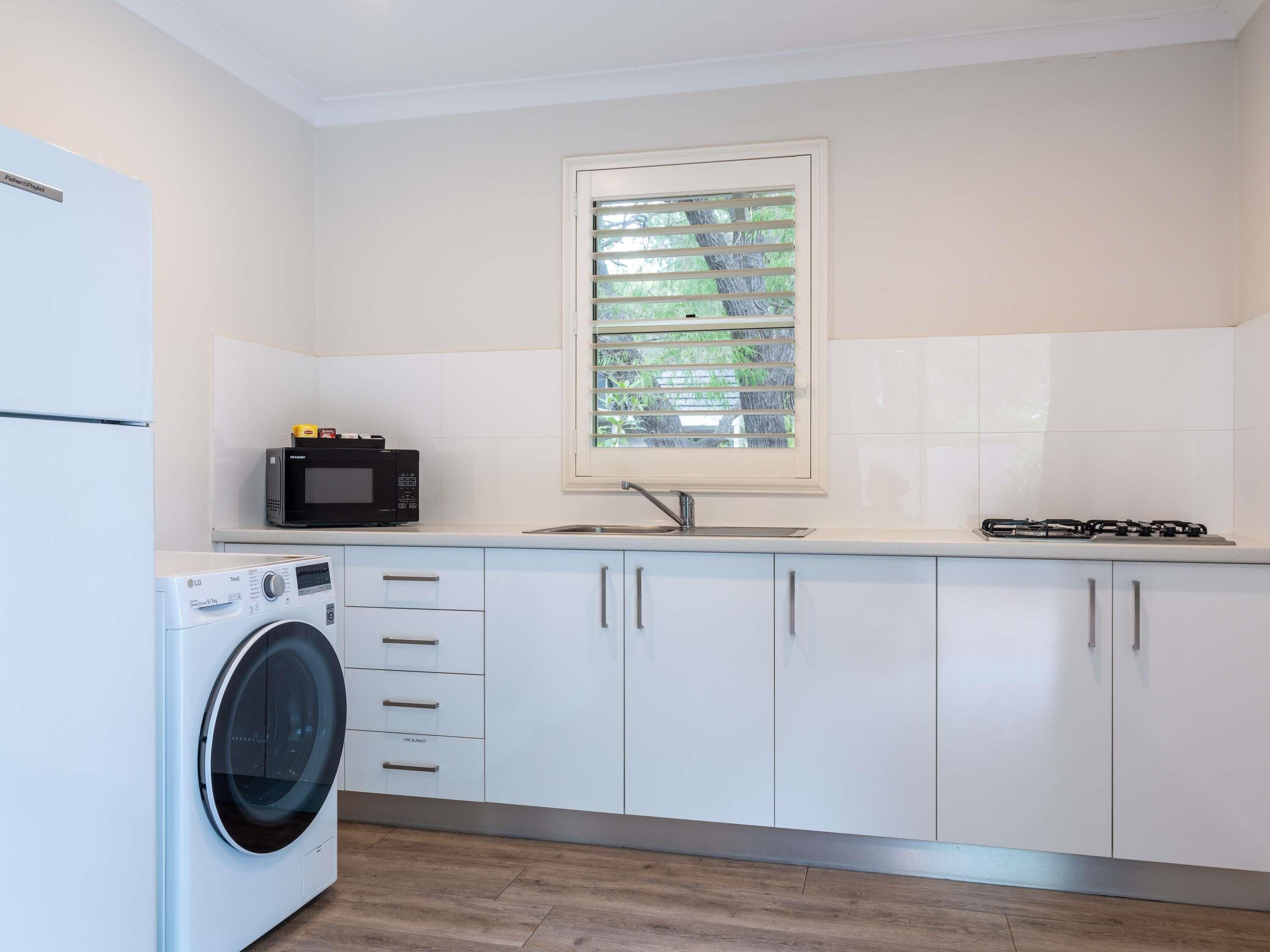 A modern kitchen with white cabinets, a built-in washing machine, a microwave, and a gas stove.