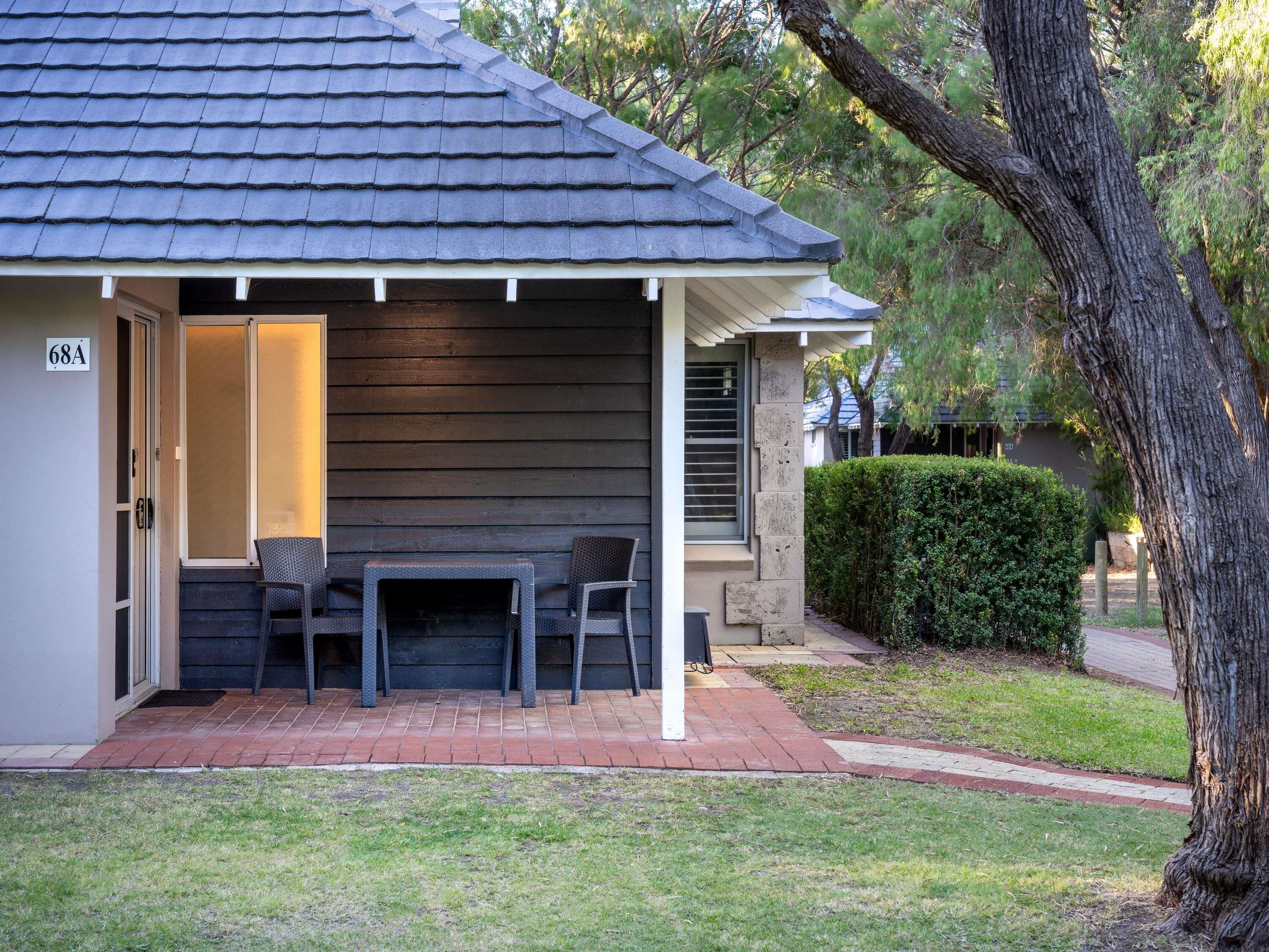 A house with a dark grey roof, a small porch with two chairs, and a hedge in the background.