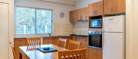 Una cocina con armarios de madera, estufa, microondas, horno y una mesa de comedor con sillas.