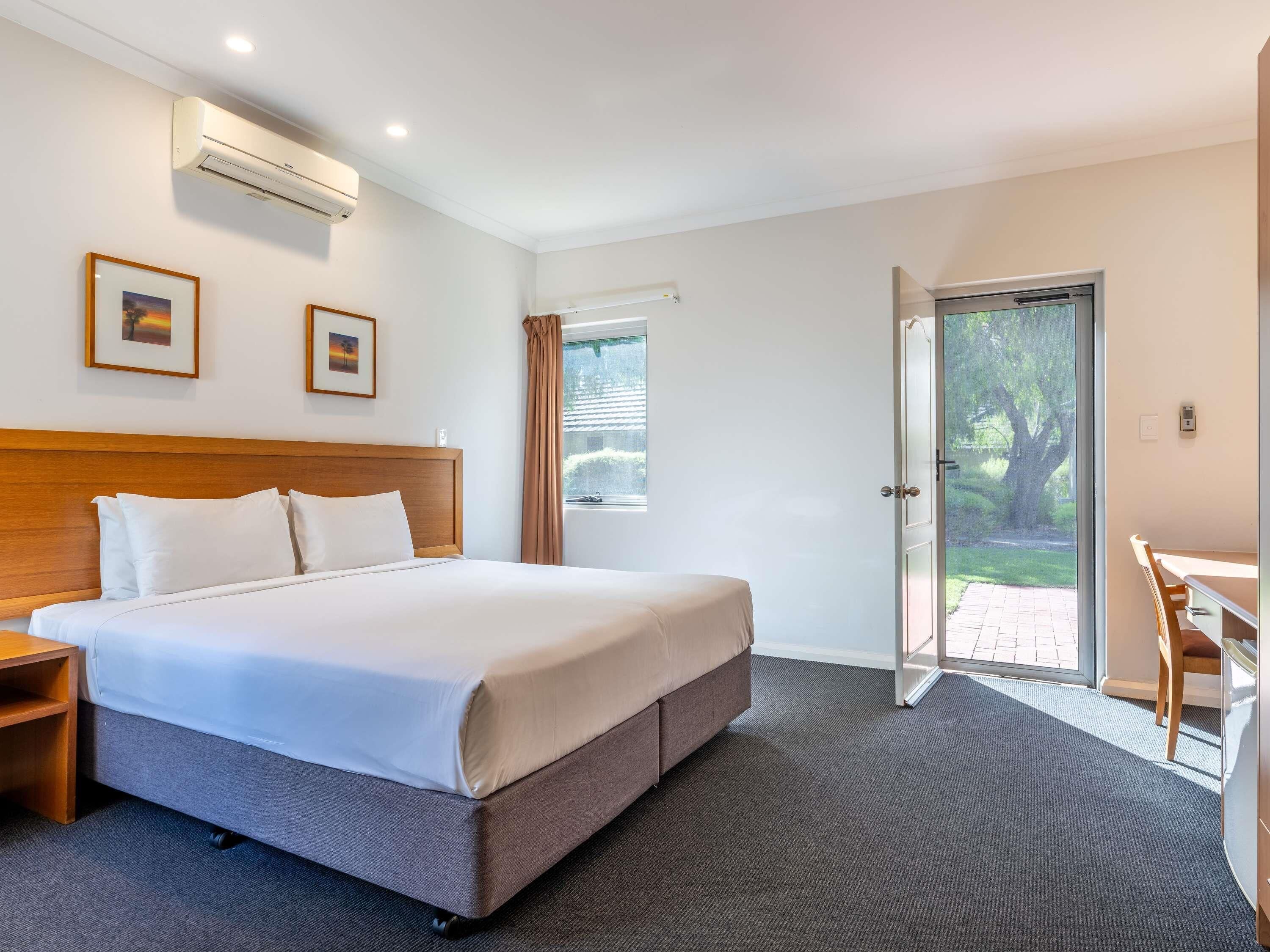 Habitación de hotel con una cama grande, un escritorio y una puerta que da a un espacio exterior.