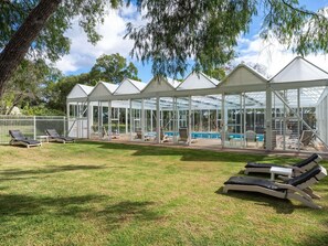 A covered outdoor area with lounge chairs, a pool, and a glass-enclosed structure.