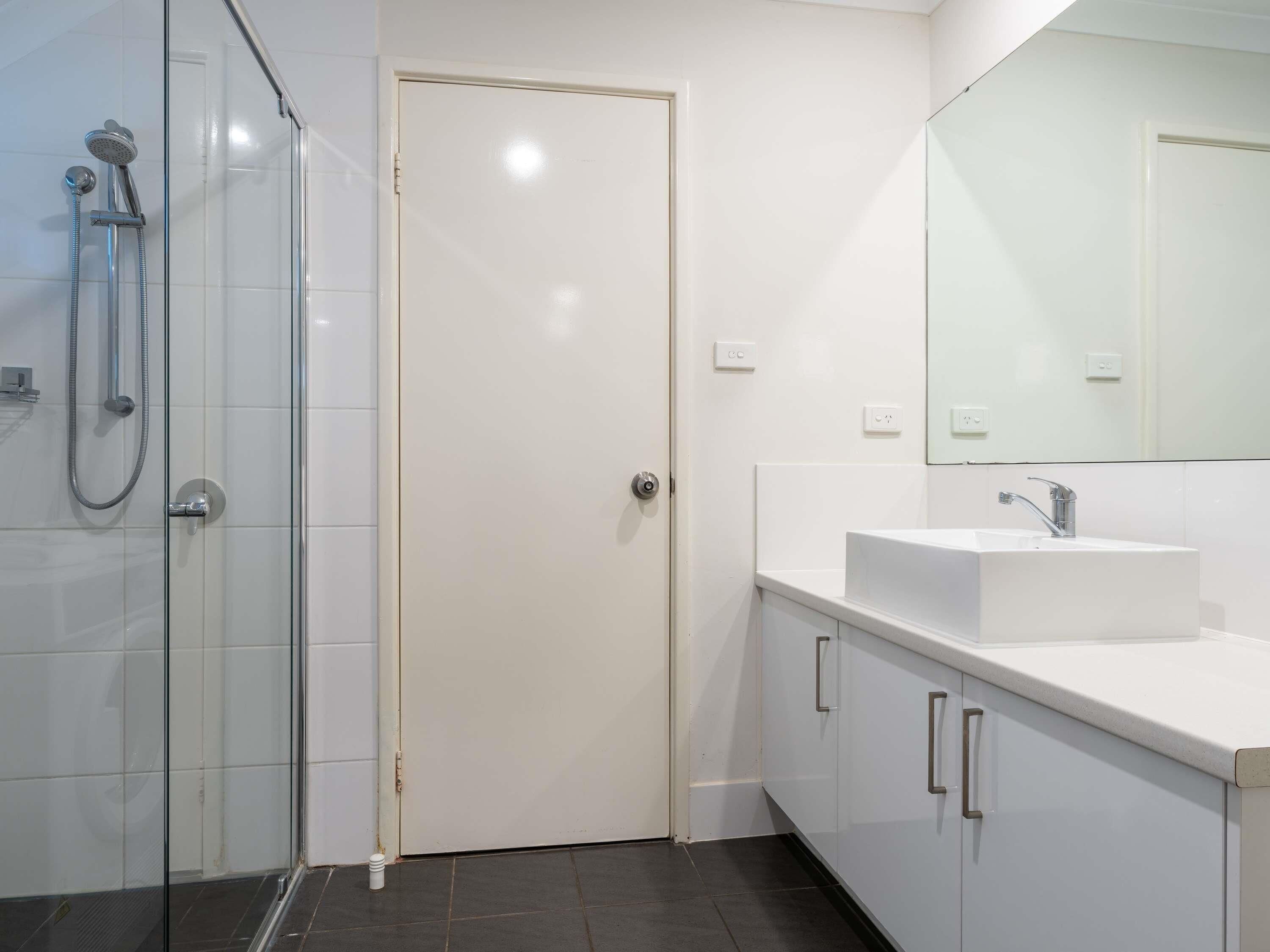 A bathroom with a glass shower enclosure, a white sink, and a mirror above the sink.