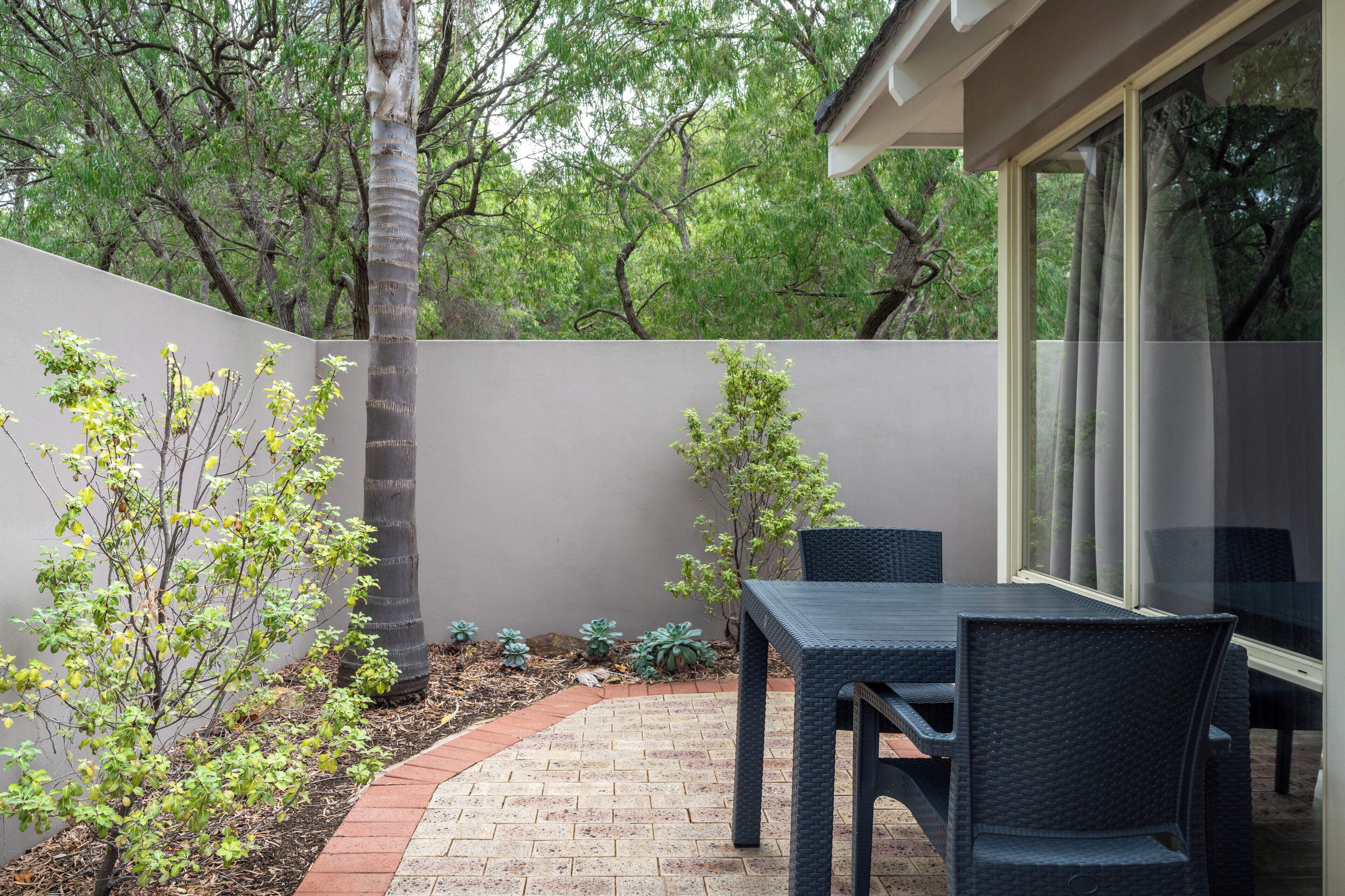 A patio with a table and chairs, surrounded by a low wall and trees.