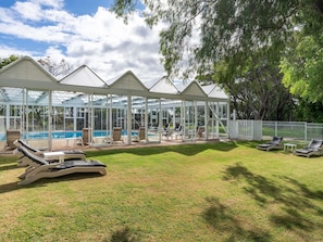 A covered outdoor swimming area with lounge chairs and a pool.